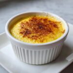 Close-up of a perfect silky egg custard in a white ramekin with a torched, caramelized sugar top.