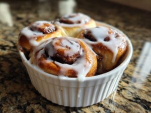 Four freshly baked small batch cinnamon rolls topped with thick white icing, nestled in a white fluted ramekin.