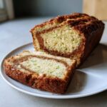 A loaf of snickerdoodle zucchini bread, partially sliced, showing a prominent cinnamon swirl inside.