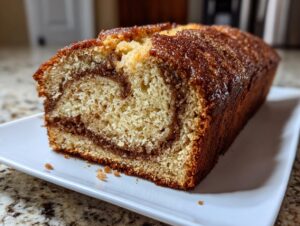 A close-up of a freshly baked snickerdoodle zucchini bread loaf, showing a moist crumb and a dark cinnamon swirl.