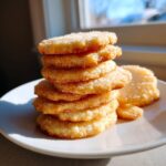 A tall stack of soft, thick sugar cookies coated in sparkling cinnamon sugar, sitting on a white plate.