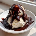 Two scoops of vanilla ice cream generously covered in homemade chocolate syrup in a white bowl.