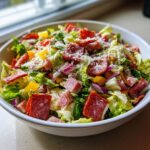 A close-up of a vibrant grinder salad filled with lettuce, pepperoni, ham, peppers, red onion, and grated cheese.