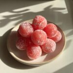 A small stack of bright pink, round watermelon mochi dusted lightly with powdered sugar on a ceramic plate.