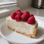 A slice of creamy white chocolate mousse tart with a graham cracker crust, topped generously with fresh raspberries.