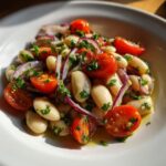 Close-up of a zesty white bean salad featuring cannellini beans, halved cherry tomatoes, and sliced red onion, dressed in oil and herbs.