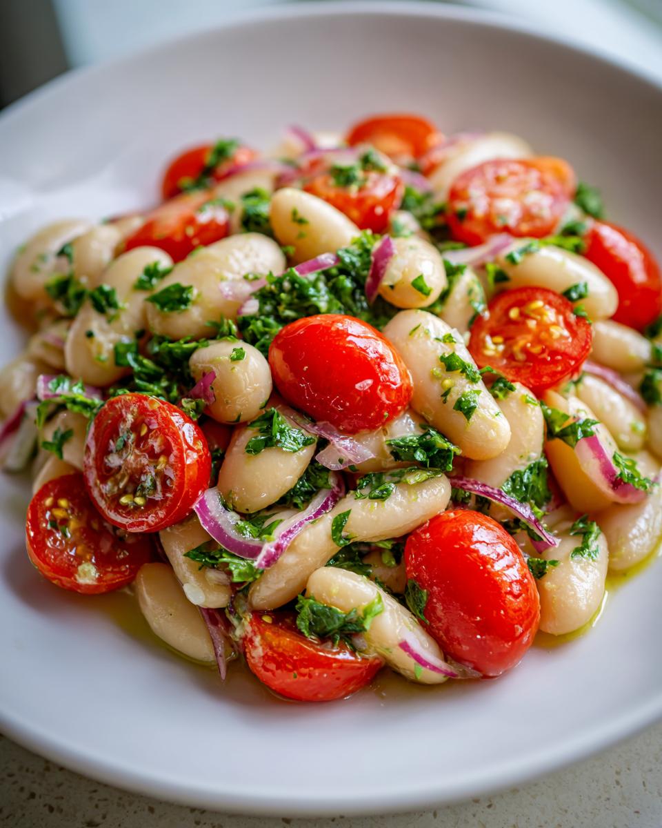 Close-up of a vibrant white bean salad featuring cannellini beans, halved cherry tomatoes, red onion, and fresh herbs.