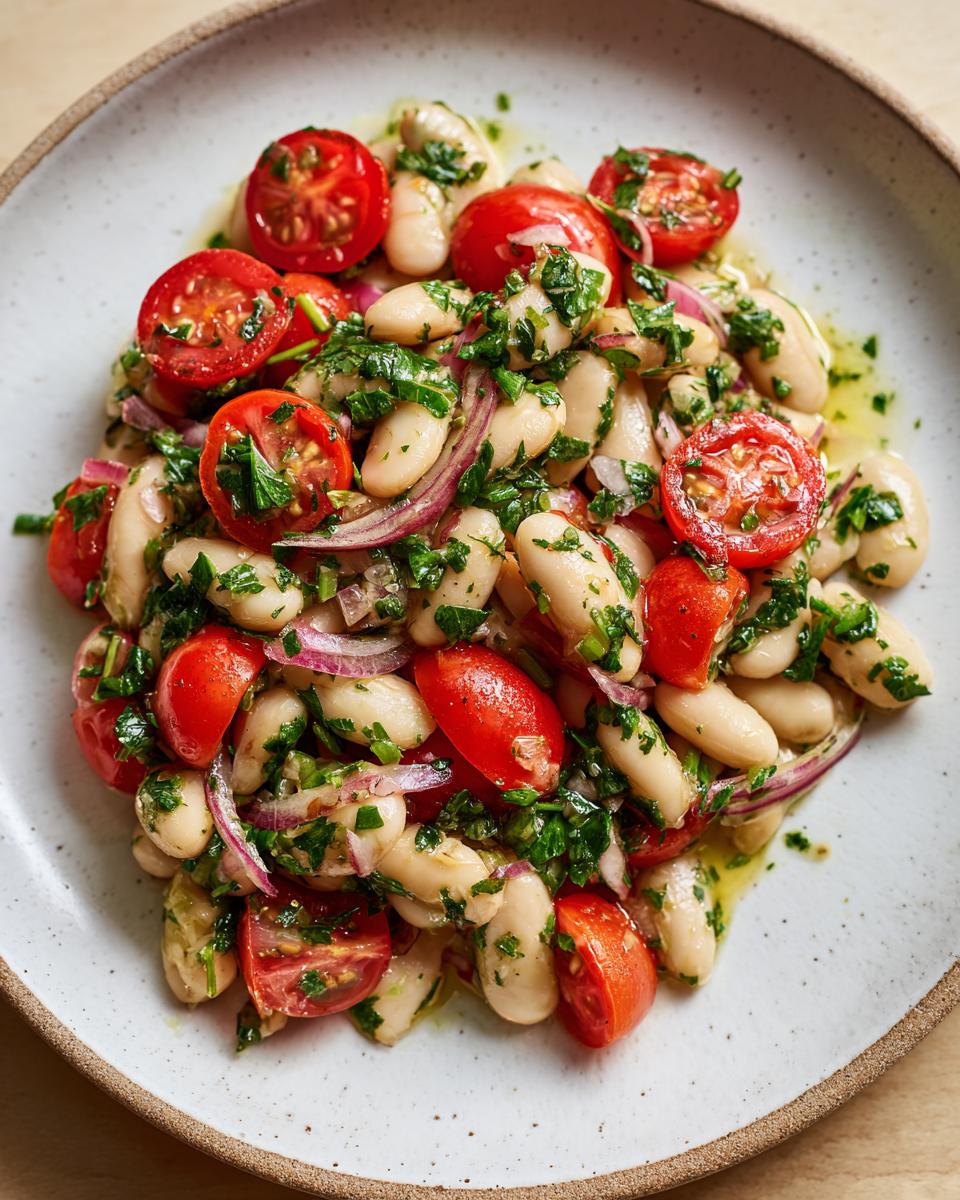 Close-up of a vibrant white bean salad mixed with halved cherry tomatoes, red onion, and fresh parsley.
