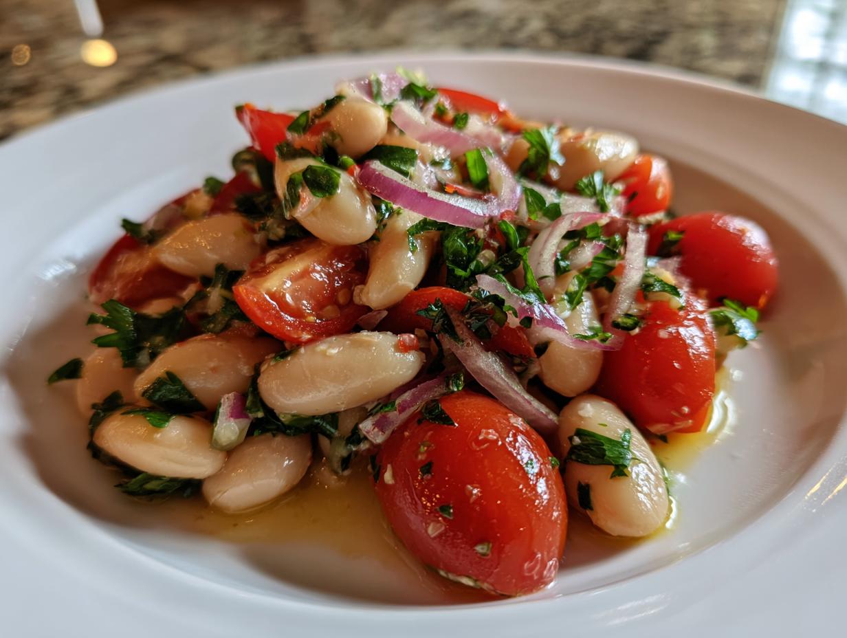 Close-up of a vibrant white bean salad featuring cannellini beans, halved cherry tomatoes, red onion slices, and fresh parsley.