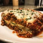 A close-up of a hearty slice of zucchini lasagna layered with meat sauce and melted cheese, garnished with parsley.